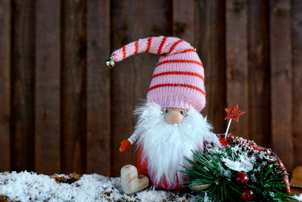 A cute Christmas gnome with a striped hat sits among snow and festive decorations.
